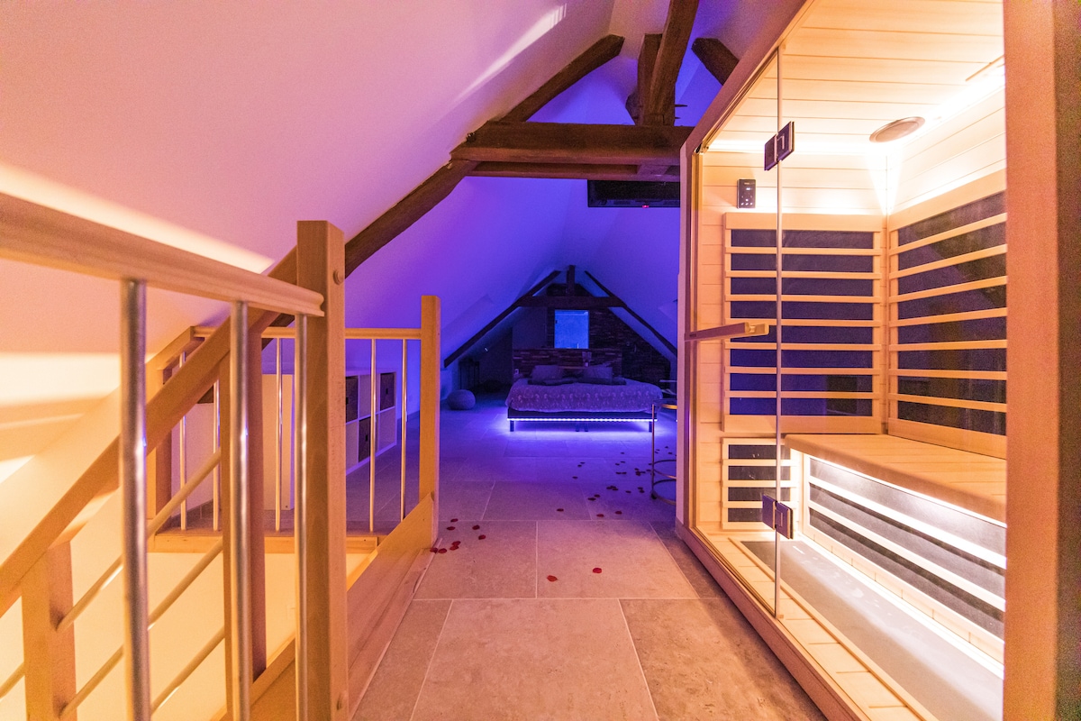 A serene wellness area is showcased with a wooden sauna on one side and a relaxation space featuring a comfortable lounge bed. Soft, ambient lighting enhances a tranquil atmosphere, while wooden beams offer architectural interest across the ceiling.