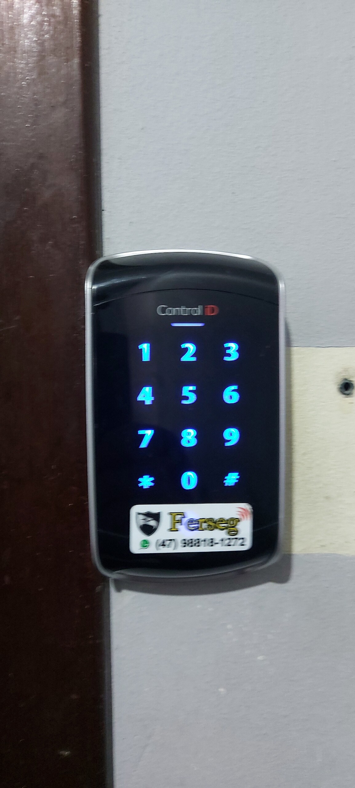 An electronic keypad lock is mounted on the wall, featuring a numeric display with illuminated blue numbers. A small sticker with contact information is situated at the bottom of the keypad. This lock design allows for secure access without traditional keys.