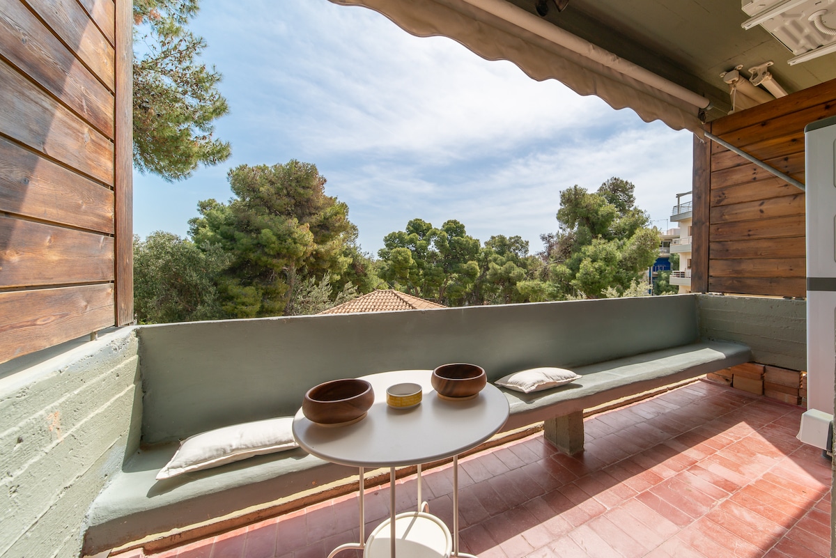 An outdoor seating area features a low, cushioned bench along a wall and a small, round table. Two bowls are placed on the table, and greenery can be seen in the background, suggesting a serene atmosphere.