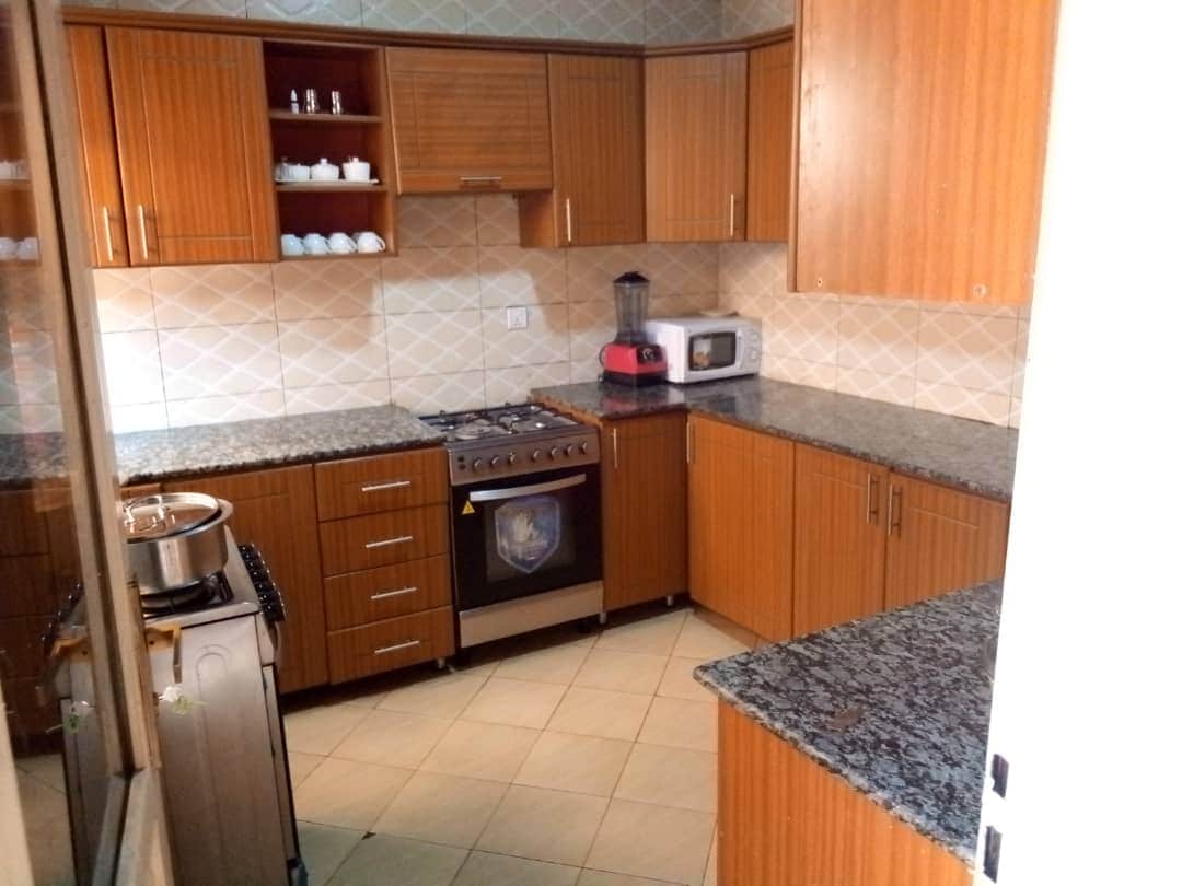 A modern kitchen features wooden cabinetry and a granite countertop. Stainless steel appliances include a gas stove and microwave. Clean lines and ample storage space enhance functionality. The tiled floor is complemented by a mix of neutral tones throughout the space.