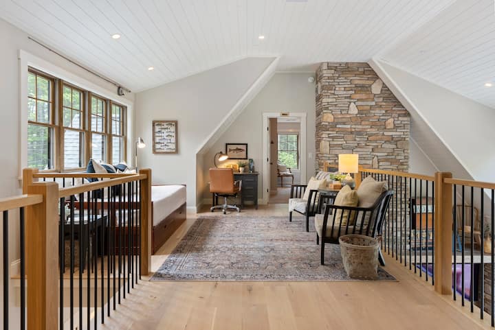 Loftový priestor s písacím stolom, dennou posteľou a priestorom na posedenie s výhľadom na jazero cez okná 