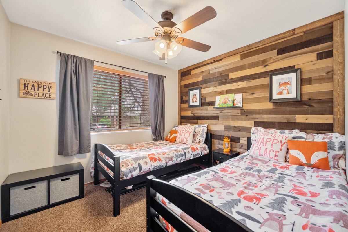 Habitación de invitados con 2 cómodas camas individuales y ventilador de techo. Los contenedores están llenos de libros para niños de todas las edades