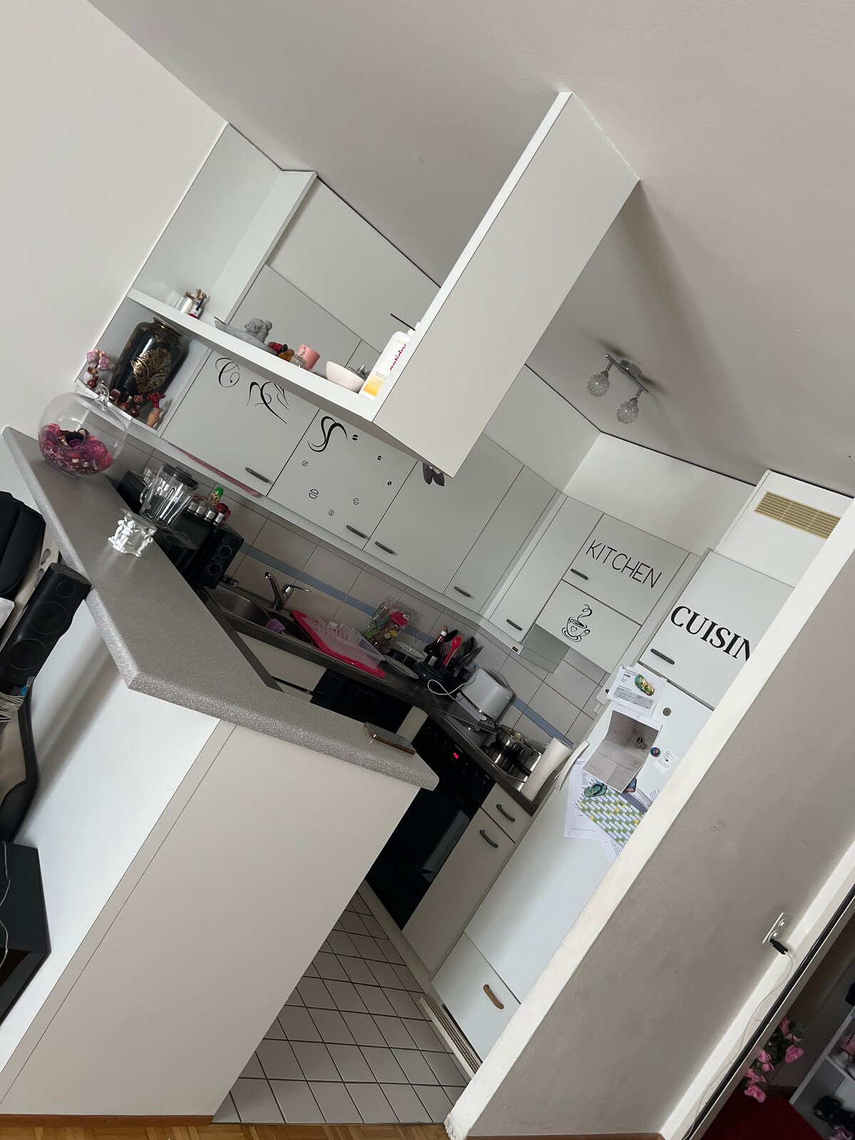 A compact kitchen is equipped with modern appliances and ample storage. White cabinetry contrasts with a gray countertop. A refrigerator and black appliances are visible, alongside decorative items on the counter, creating a functional cooking space.