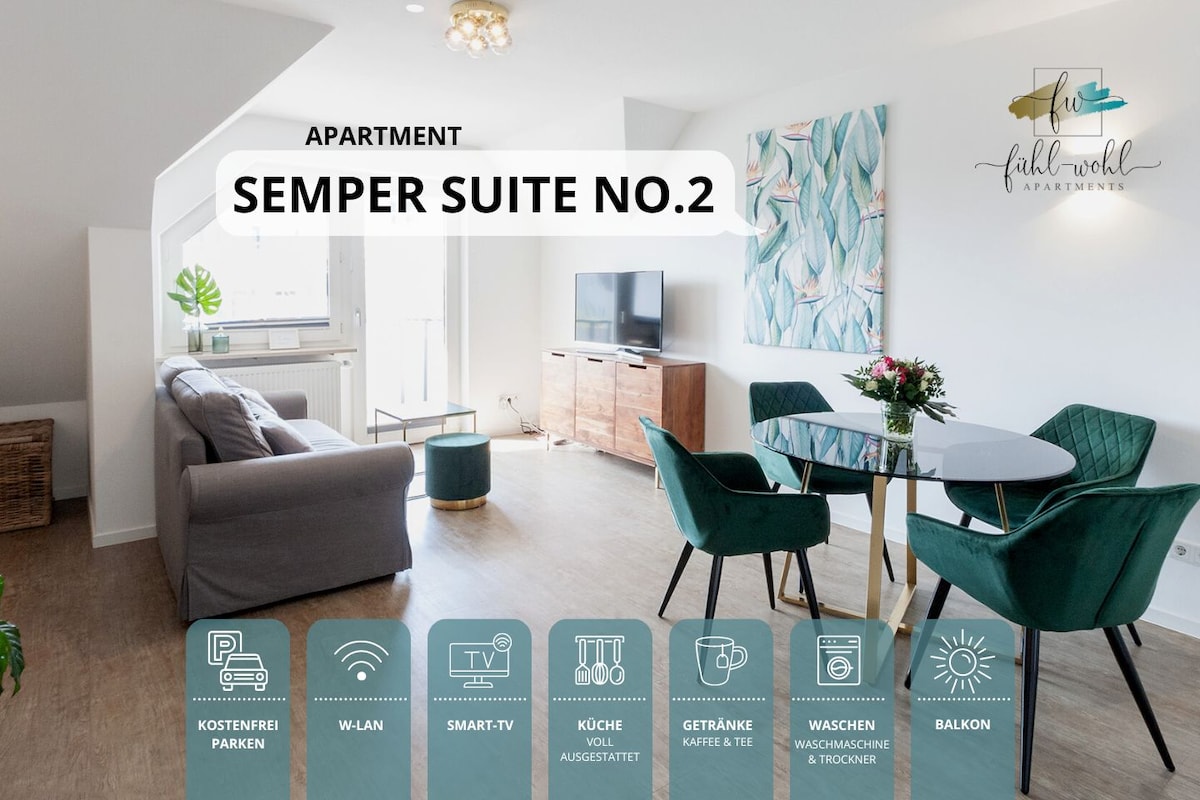 A spacious living area features a light-filled ambiance with large windows. Modern furnishings include a comfortable sofa and a dining table. A decorative wall art piece adds a touch of style, while a balcony is accessible for outdoor relaxation.