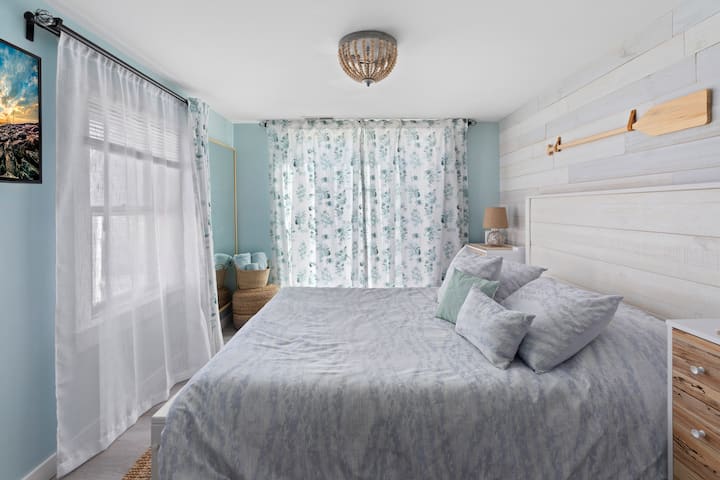 Tercer dormitorio con una cama tamaño queen y mucha luz natural. Puerta corrediza abierta a la cubierta trasera (al lado de la calle). Junto a este dormitorio hay un medio baño renovado. 