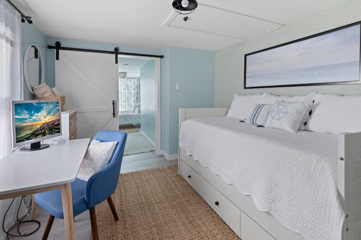 Cuarto dormitorio con cama nido doble. Este es un dormitorio de paso donde se puede ver el tercer dormitorio más allá de la puerta del granero. El medio baño se encuentra entre las dos habitaciones. También hay un escritorio y una pantalla de computadora para fines de trabajo.  