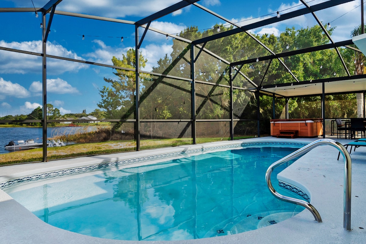 A screened-in lanai features a sparkling pool beside a tranquil lake. The hot tub is visible nearby, offering a relaxing space. Lush greenery frames the view, while outdoor seating can be seen, providing a perfect setting for leisure and enjoyment.