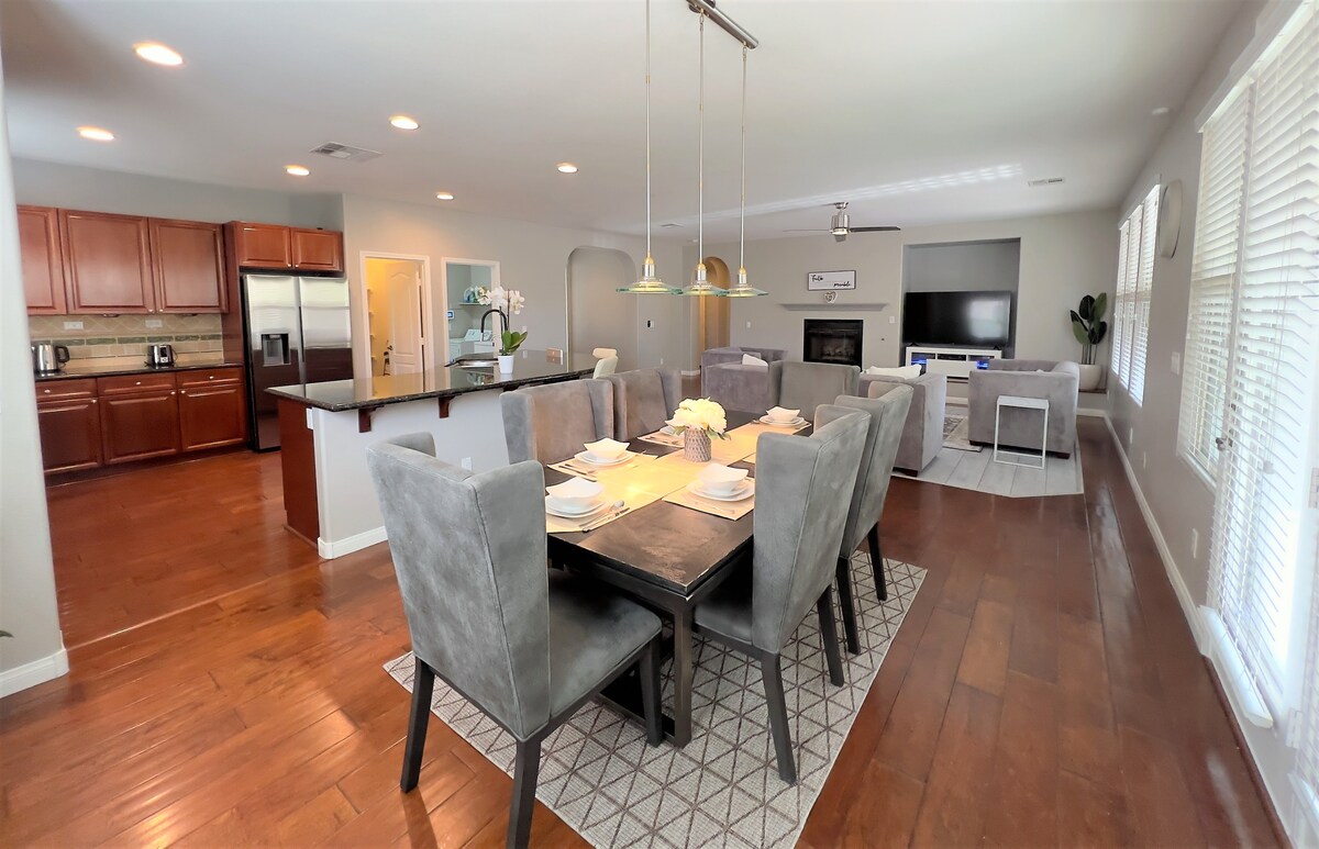 A spacious open-concept living and dining area features a large dining table set for a meal, surrounded by plush gray chairs. The adjacent kitchen is equipped with dark wood cabinetry and stainless steel appliances, creating an inviting environment for gatherings.