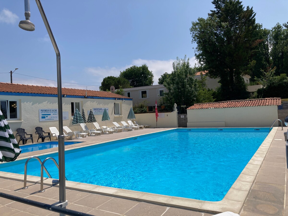 A refreshing outdoor pool is surrounded by lounge chairs featuring striped umbrellas. The pool area is well-maintained, with a vibrant blue water surface reflecting the clear sky. Trees and buildings provide a calm backdrop, enhancing the inviting atmosphere of the swimming space.