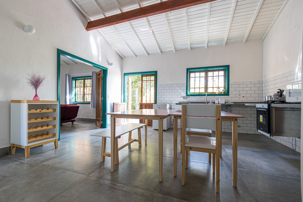 A spacious kitchen area is showcased, featuring a wooden dining table with matching chairs, set against light-colored walls. The kitchen includes a stove and countertop, with ample natural light filtering through multiple windows. A vibrant arrangement sits on the table, adding a subtle touch of color.
