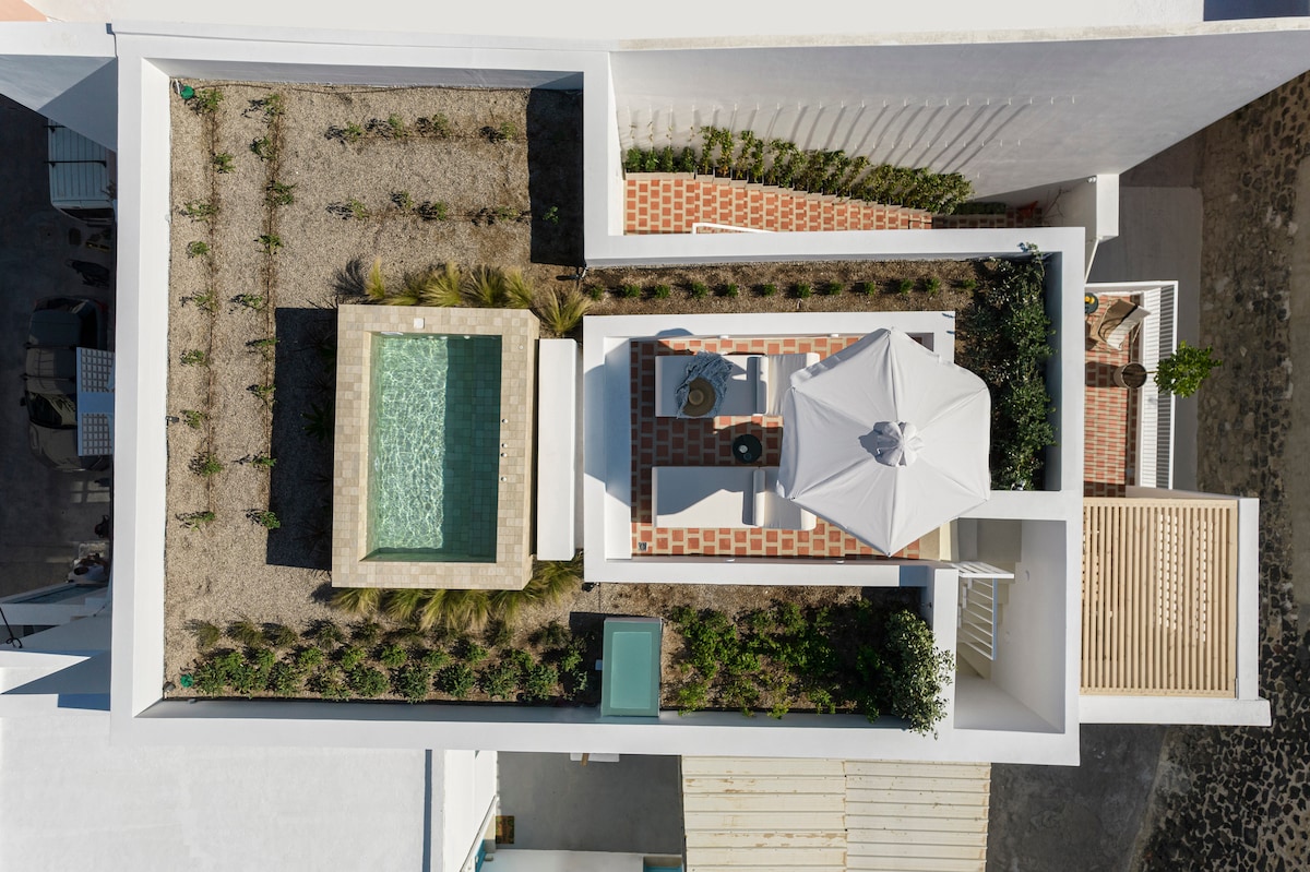 An aerial view reveals a private outdoor area featuring a small pool surrounded by stone pathways and landscaped greenery. Comfortable seating options are positioned under a white umbrella, while terracotta tiles provide texture to the space.