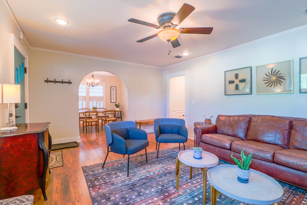 Seating is arranged in a welcoming living room, featuring a brown leather sofa and two blue accent chairs. A small table holds a potted plant. Light fixtures illuminate the space, highlighting the hardwood floors and decorative area rug.