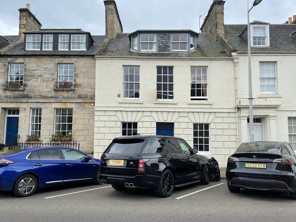 A classic townhome features a symmetrical facade with large windows. The upper floor is highlighted by three windows, providing ample natural light. Parked vehicles, including a black SUV and a blue car, occupy the space in front of the property, illustrating convenient on-street parking.