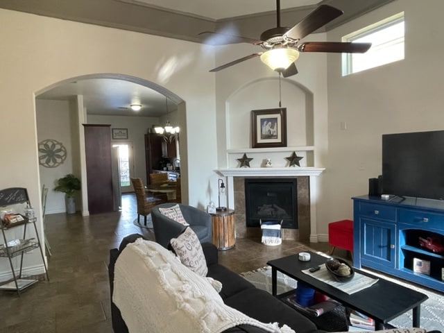 The open living area features a cozy seating arrangement, with a dark sofa and coffee table placed near a built-in gas fireplace. A ceiling fan offers ventilation, and a large smart TV is positioned next to a vibrant blue media console. Natural light streams through large windows.