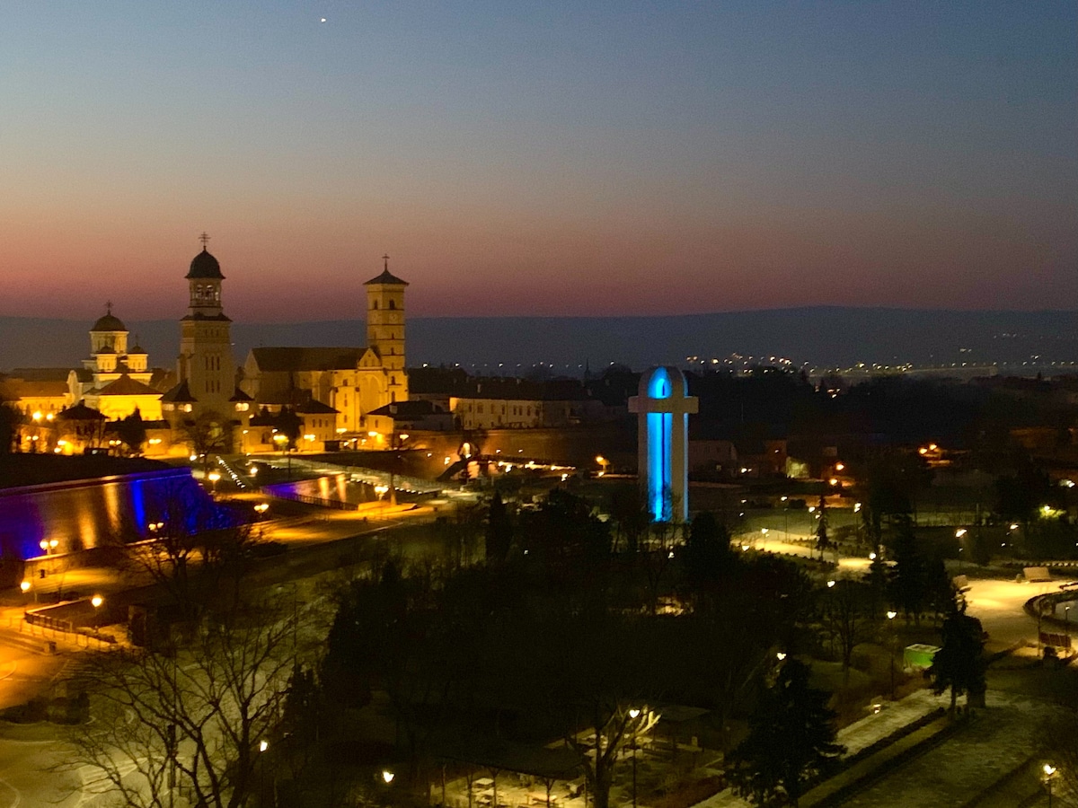 An evening view features illuminated buildings, showcasing the Reunification and Roman Catholic Cathedrals against a twilight sky. The landscape is complemented by a city park, where soft lighting highlights pathways and trees, creating a serene atmosphere.
