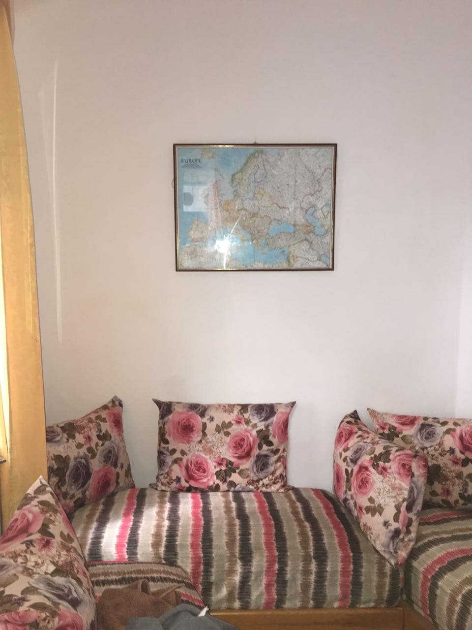 A seating area features a low, cushioned bench adorned with floral-patterned pillows in shades of pink and brown. A vintage map is framed and displayed on the wall above the seating, adding an element of interest to the space.