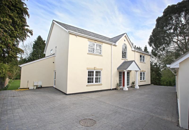 The exterior of a spacious two-story home is displayed, featuring a light-colored facade and a symmetrical design. A welcoming entryway is framed by a small porch, while a paved driveway offers ample parking space and leads to a surrounding greenery.