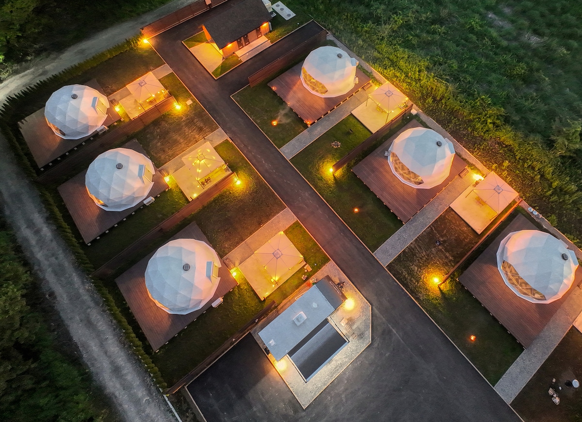Aerial view of the glamping resort displays multiple dome-shaped tents, surrounded by illuminated pathways. Each tent is set within a spacious area, enhancing the outdoor experience. Soft lights create a warm ambiance, highlighting the landscaped surroundings.
