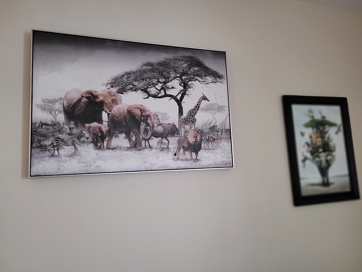 A vibrant wall is adorned with two framed artworks. One frame displays a monochrome scene of elephants, a giraffe, and zebras under a large tree, while the other features a floral arrangement in a decorative vase.