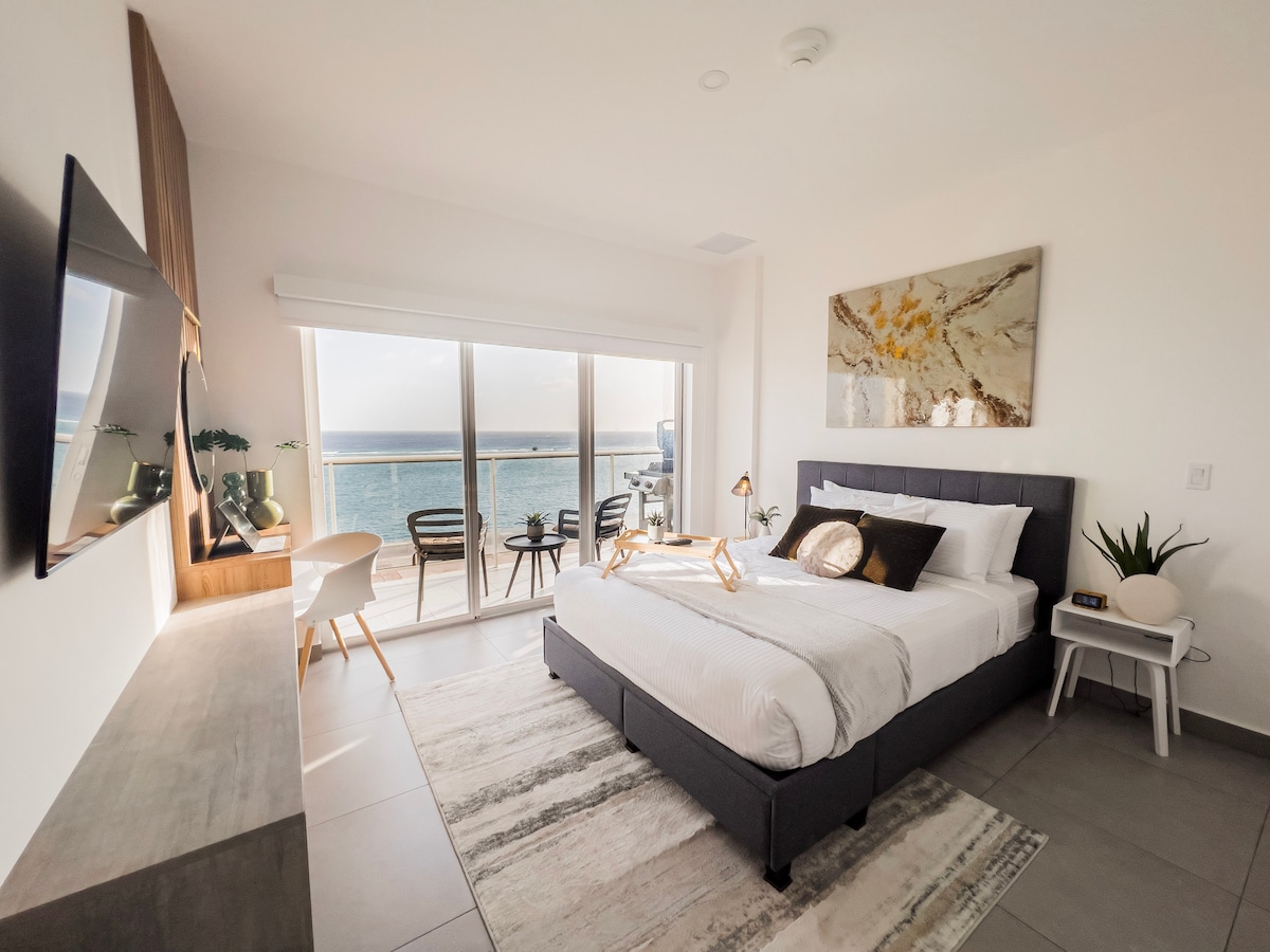El segundo dormitorio tiene una cama tamaño queen, unidad de pared de diseño personalizado, altavoz Bluetooth, TV de 42 pulgadas con IPTV y acceso al balcón a las vistas al mar que nunca olvidarás.  Alexia Echo Dot