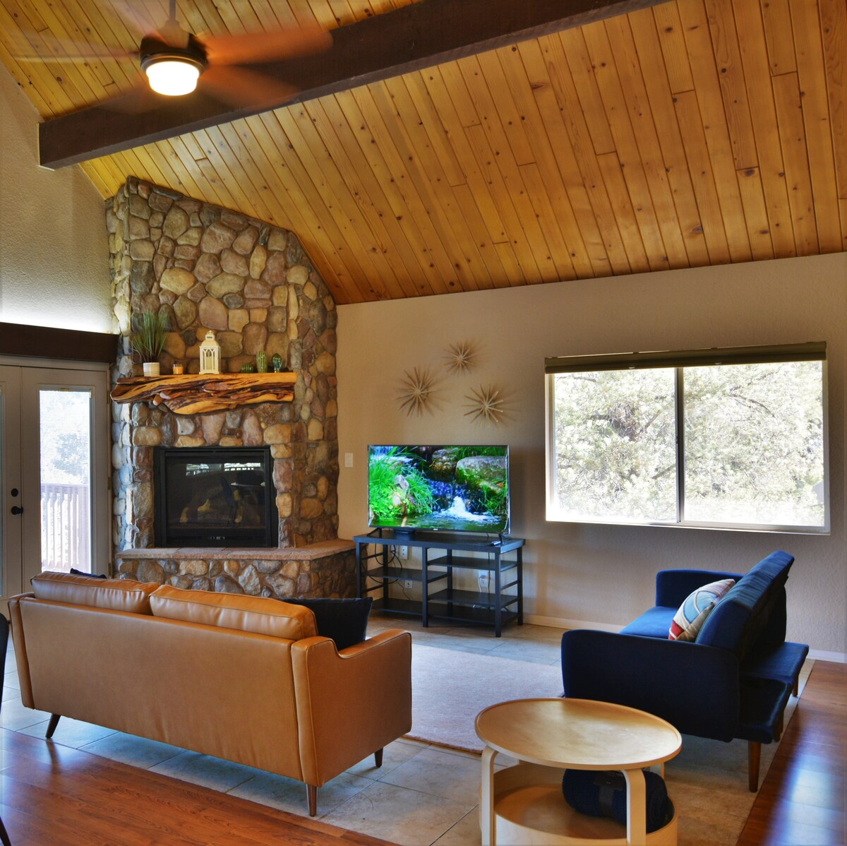 The large river rock fireplace reaching high to the vaulted ceiling, with each carefully placed rock and artisan finished natural wood mantle make it a unique focal point and cozy gathering point with seating provided by two firm formal sofas.
