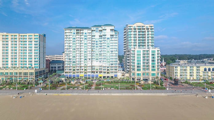 A view of the resort's oceanfront buildings showcases an inviting atmosphere with modern architecture. The sandy beach lies in the foreground, while well-maintained pathways and landscaped gardens can be seen to enhance the outdoor space, providing easy access to the ocean.