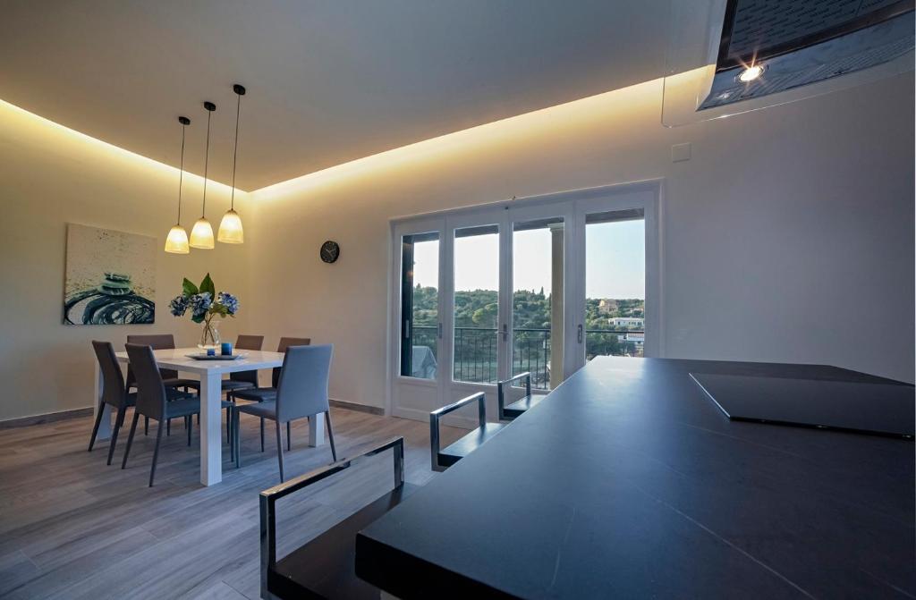 A dining area features a modern table surrounded by six chairs, with two pendant lights illuminating the space. Sliding glass doors provide scenic views of the outdoor landscape while a simple floral arrangement sits at the center of the table.