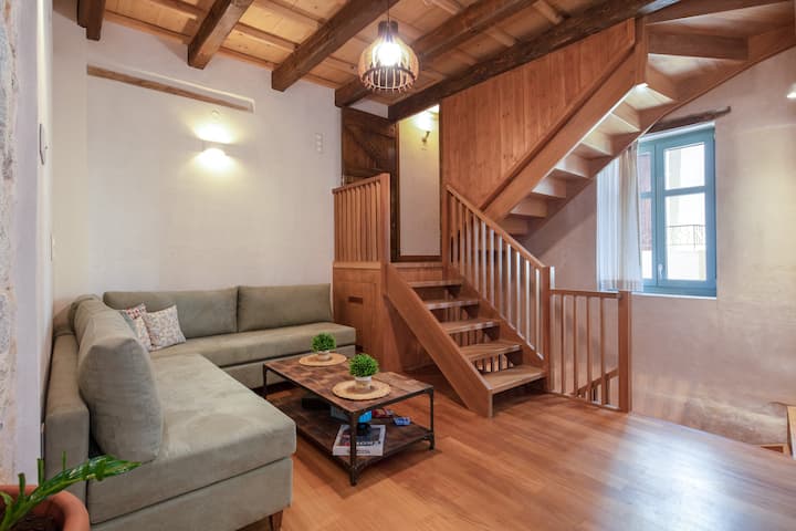 Първият етаж, с хладно дървено стълбище, сив уютен диван и дървената малка маса за почивка