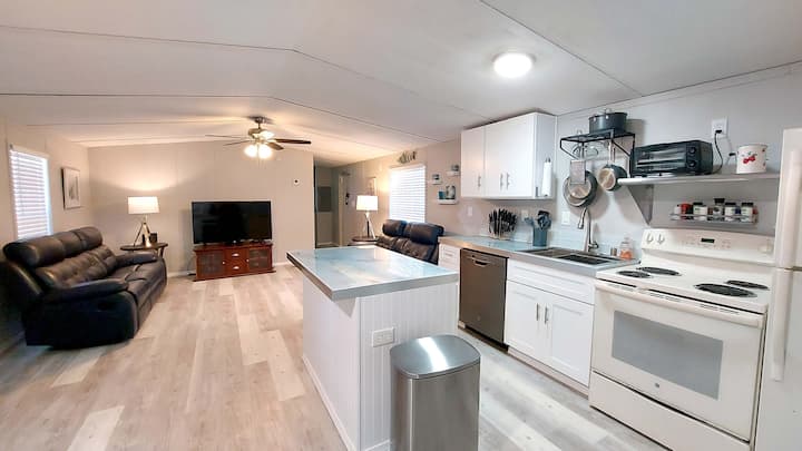 Ambienti i kuzhinës së ndenjjes me divan lëkure të mbështetur dhe ndenjëse dashurie, televizor Android dhe ventilator tavani.