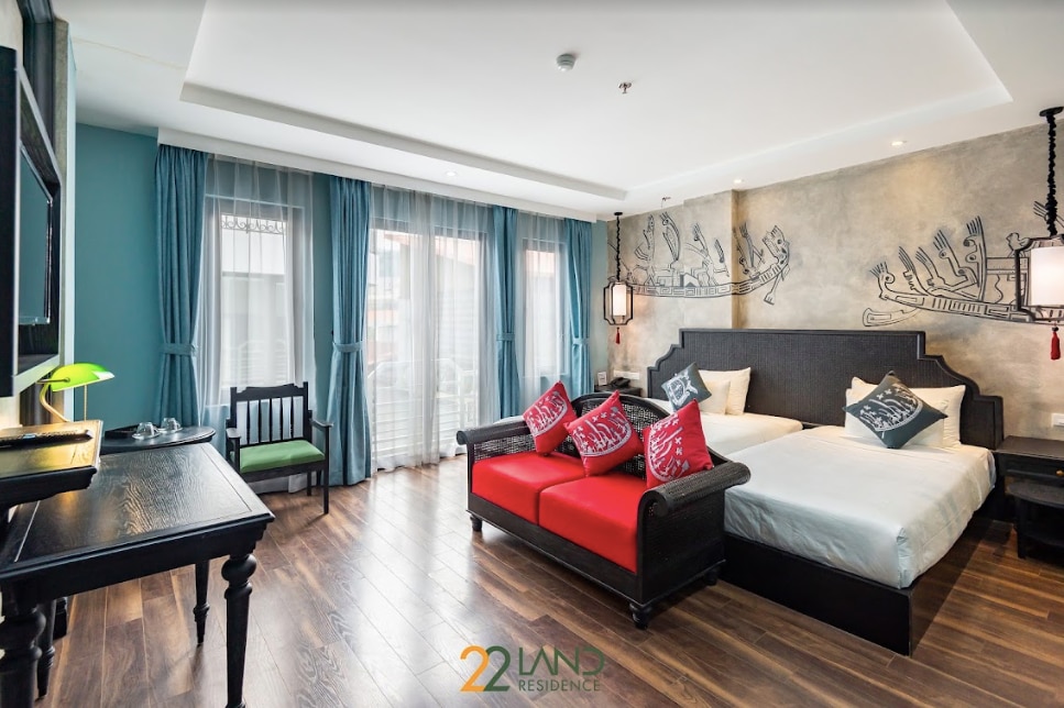 A well-appointed guest room is presented with a spacious bed and a separate sleeping area. Decorative pillows adorn the red accent sofa. Natural light filters through the sheer curtains, enhancing the room's inviting look, while artistic wall designs add a unique touch.