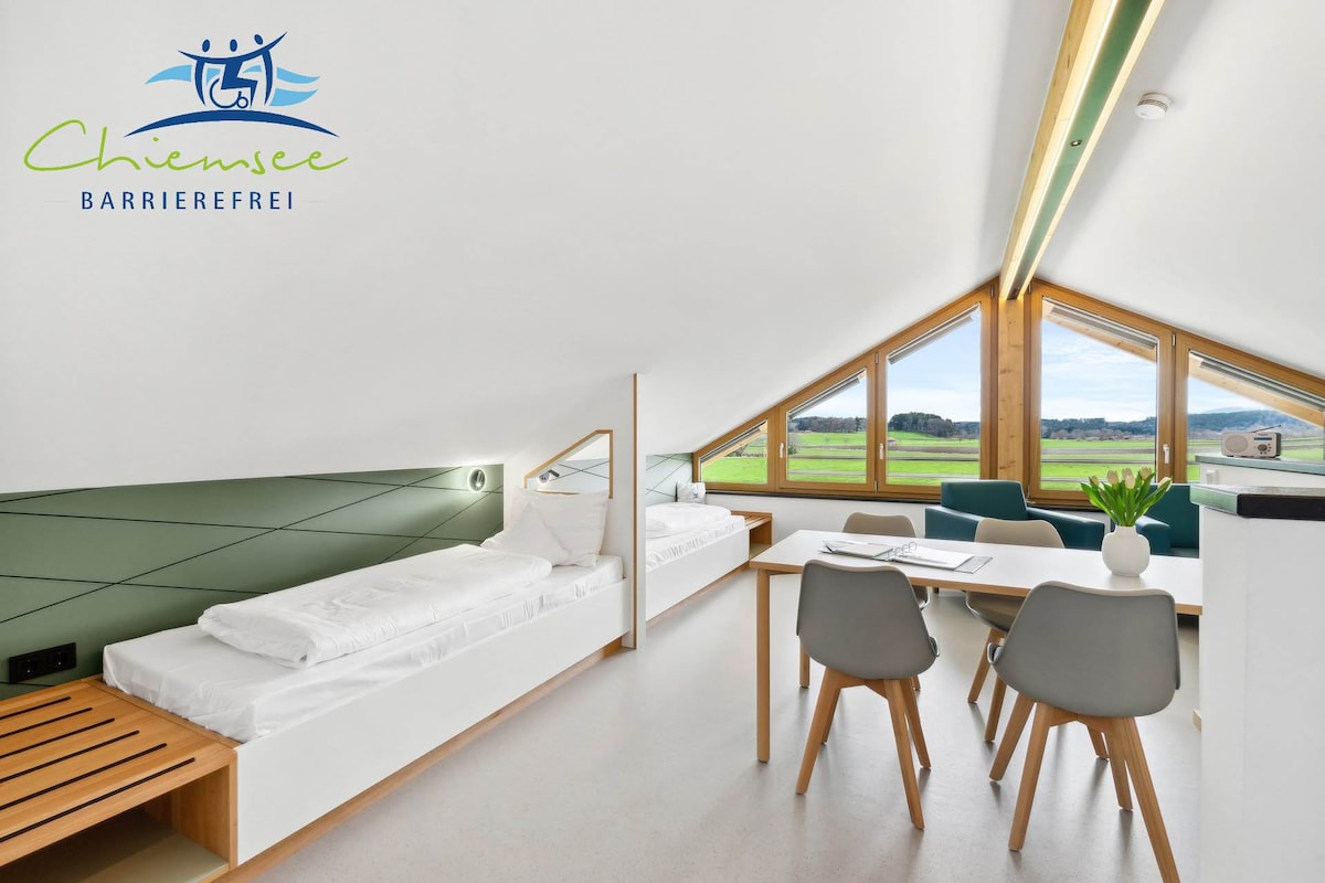 The light-filled room features large triangular windows that provide scenic views of the surrounding landscape. A spacious table is surrounded by modern chairs, while two beds are neatly arranged along one wall, enhancing the room's open and airy feel.