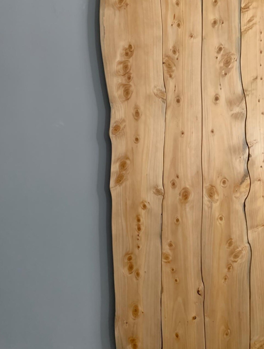 Natural wood paneling features smooth, light-colored grain patterns and knots, contrasting with the adjacent muted gray wall. The unique contours of the wood add a touch of organic charm to the space.