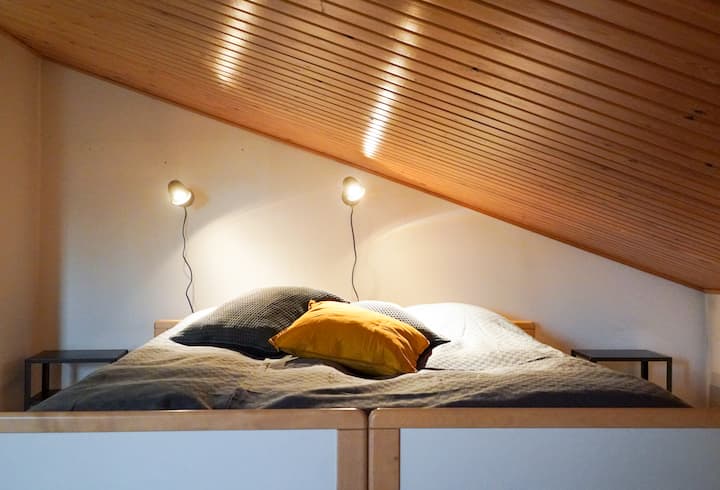 Lit double sur le loft : plafond en bois chaud, éclairage doux et literie confortable en font un refuge idéal pour un sommeil réparateur.