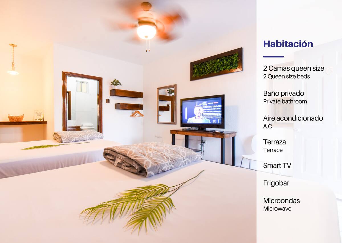 A well-appointed room features two queen-size beds, each with soft blankets. A television is mounted on the wall, and a small plant adds a touch of greenery. The room includes a private bathroom and access to a terrace, enhancing the overall comfort.