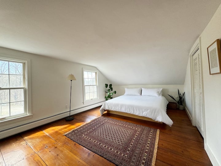 Chumba kikubwa cha kulala cha ghorofa ya juu chenye mwonekano wa kupendeza wa uwanja wa nyumba na kilima.