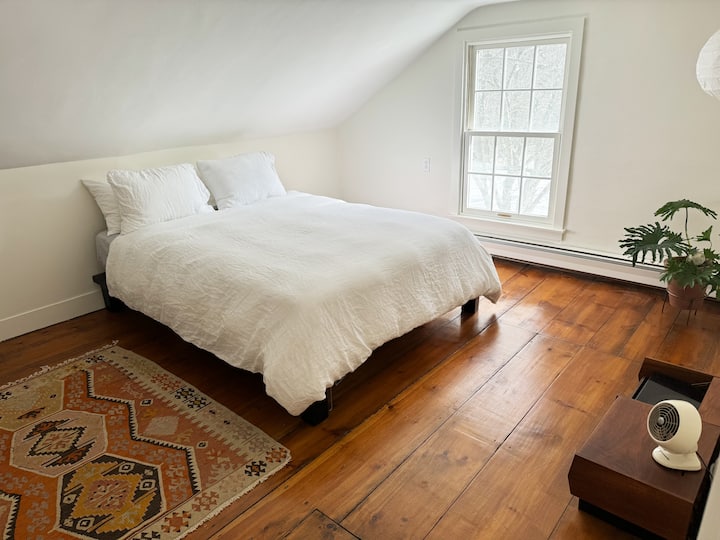 Chumba cha kulala chenye starehe cha ghorofa na kitanda cha malkia kinachoangalia bustani na mti wenye maua ya waridi.