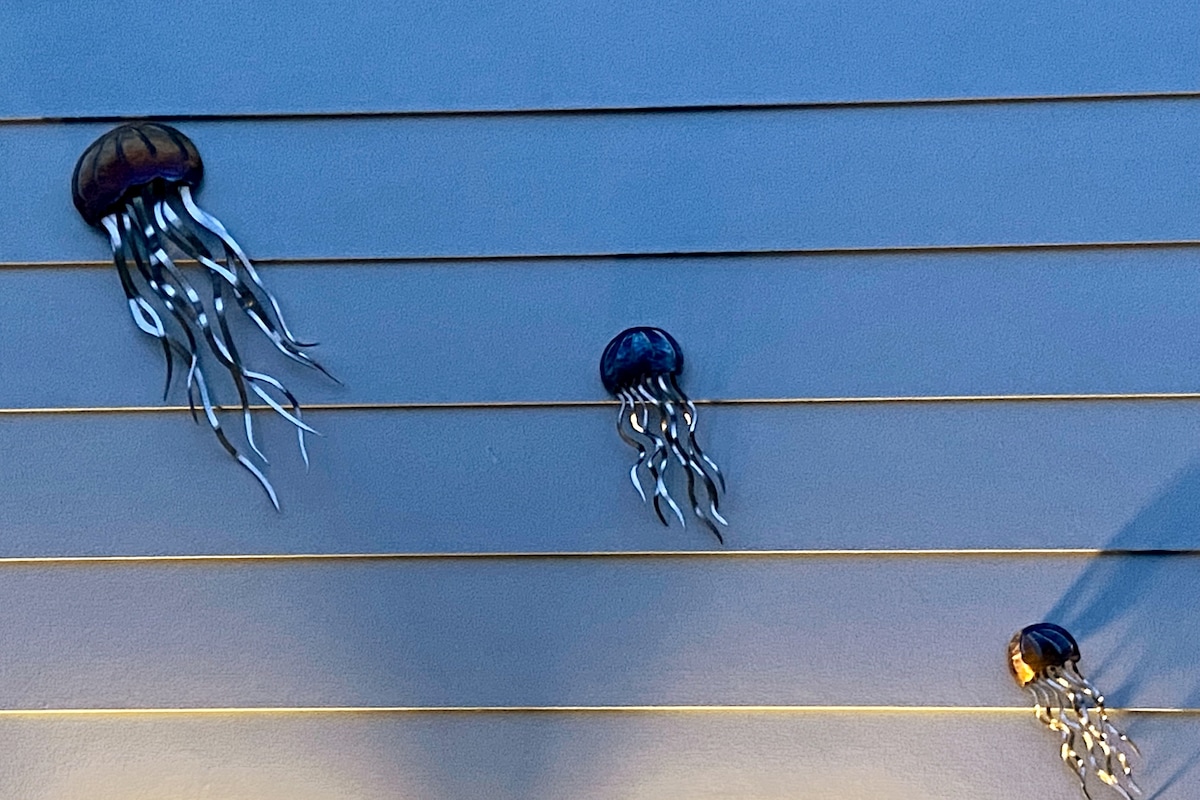 Three jellyfish sculptures are displayed against a textured blue wall. The designs feature vibrant colors and flowing tentacles, creating an artistic accent that enhances the overall ambiance of the space.