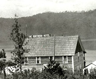 A historic wooden building is shown from an elevated angle, featuring a sloped roof and a sign that reads 'The Northern Hotel.' Surrounding trees and a distant landscape are visible, hinting at the natural scenery nearby.