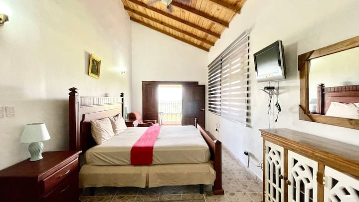 Chumba kikubwa cha kulala kilicho na bafu la kujitegemea, feni ya dari, runinga na ufikiaji wa roshani inayoangalia milima.