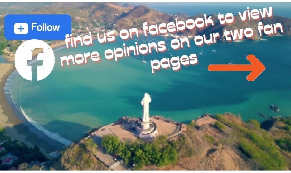 Aerial view captures a coastal landscape featuring a prominent statue overlooking a scenic bay. The water reflects various shades of blue, while sandy beaches can be seen along the shoreline, providing a serene backdrop for visitors.