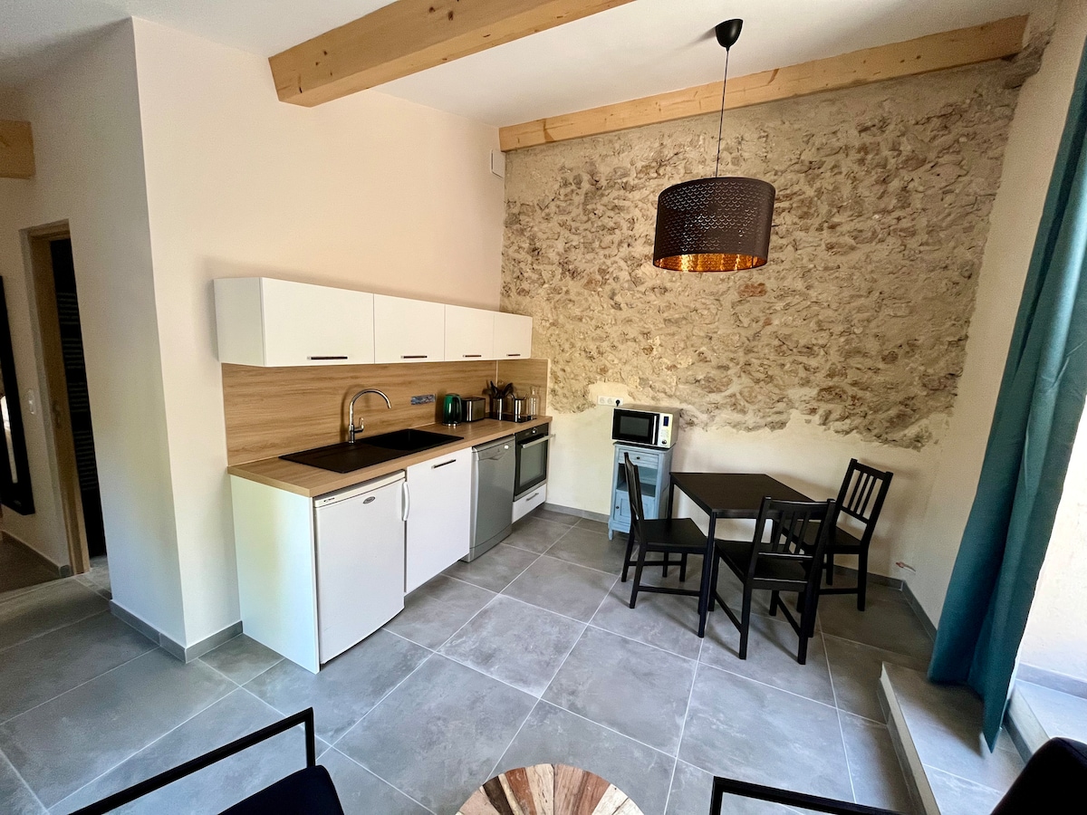 A kitchen area is presented with white cabinetry and a wooden accent wall. Appliances, including a microwave and dishwasher, are neatly arranged. A small dining table with black chairs creates a functional eating space, complemented by a pendant light that adds a modern touch.