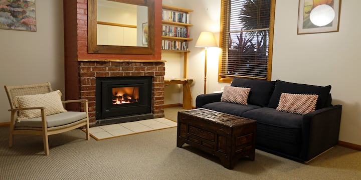 Sala de estar con chimenea de gas, sofá cama tamaño queen de tres plazas, escritorio y televisión inteligente grande.