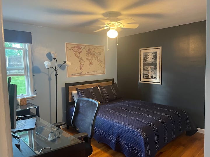 Პირველი სართულის ოთახი. საწოლი და საოფისე სივრცე, რომელიც სავსეა დიდი მოხრილი მონიტორით. 