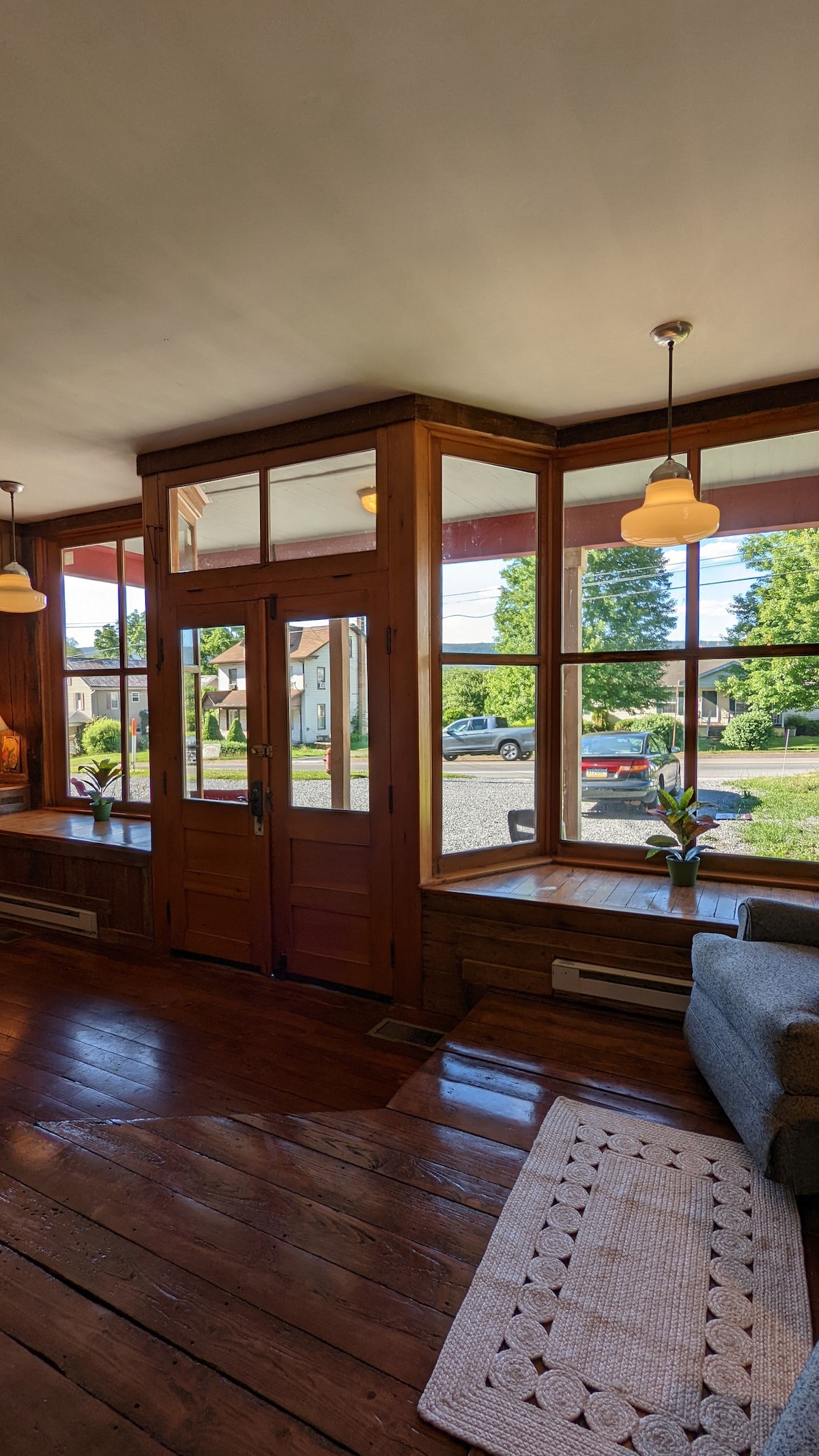 A welcoming entryway features large windows allowing natural light to fill the space. Wooden accents and polished floors create a warm atmosphere. A cozy seating area is positioned near the windows, complemented by potted plants adding a touch of greenery.