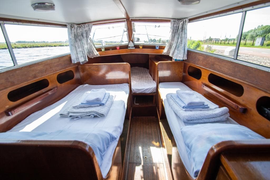 Two twin sleeping areas are positioned side by side within the wooden interior of the boathouse. Soft linens and neatly arranged towels are placed on each bed. Natural light filters through the windows, highlighting the clean surfaces and inviting design.