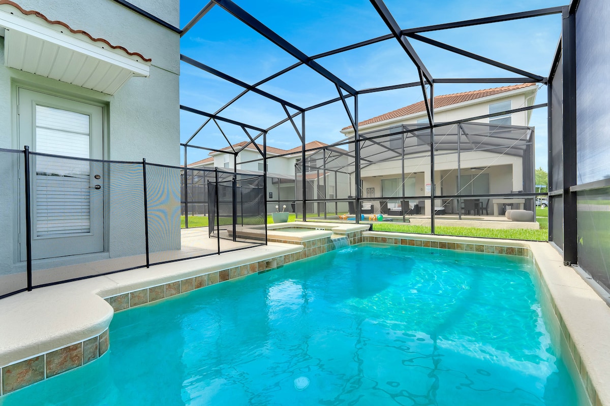 A private pool area is surrounded by a screened enclosure, showcasing clear water and a tan concrete patio. The outdoor space includes grassy areas and views of neighboring structures enhancing the sense of openness and leisure.