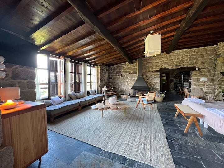 The main space of the house, enclosed by thick stone walls, and with a wide window open to the vineyard slope landscape, up to the river. The fireplace, work desk, large couch under the window and sideboard complete.