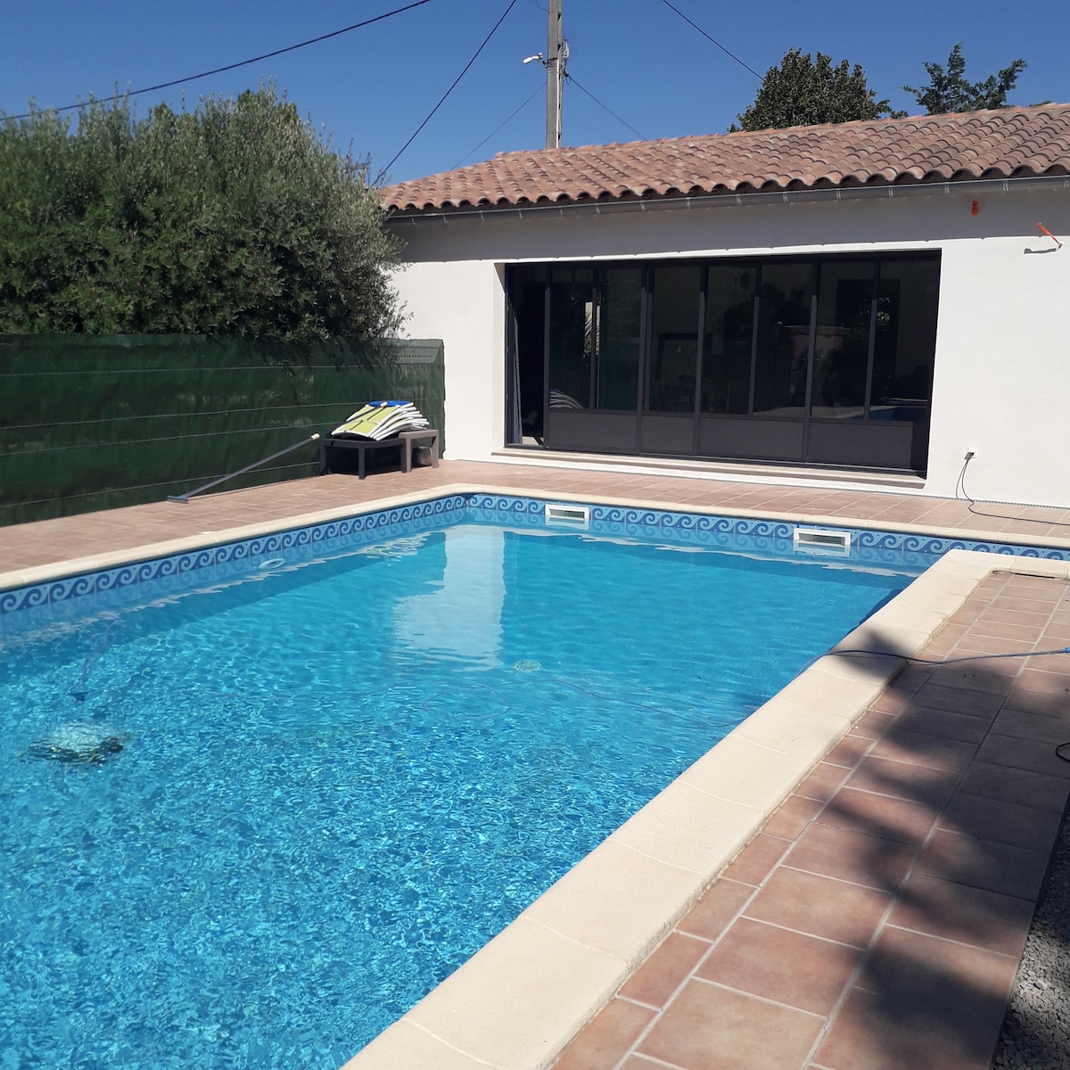 A private swimming pool measuring 10 meters in length is framed by a tiled deck. Sun loungers are arranged nearby, offering a relaxing space. Large glass doors provide a view into the living area, creating a seamless connection with the outdoor space.