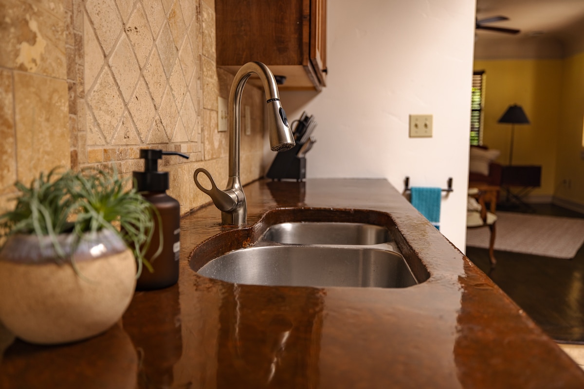 A well-maintained kitchen counter is showcased, featuring a modern sink and a sleek faucet. A small potted plant adds a touch of greenery, while a decorative soap dispenser is positioned nearby. The textured surface enhances the overall design of the kitchen area.