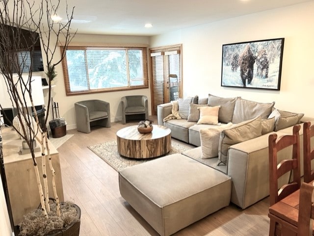 A welcoming living area is furnished with a large sectional sofa and a circular coffee table made of natural wood. Comfortable chairs are arranged for relaxation, and light enters through large windows adorned with wooden blinds. A framed wildlife artwork adds to the serene decor.